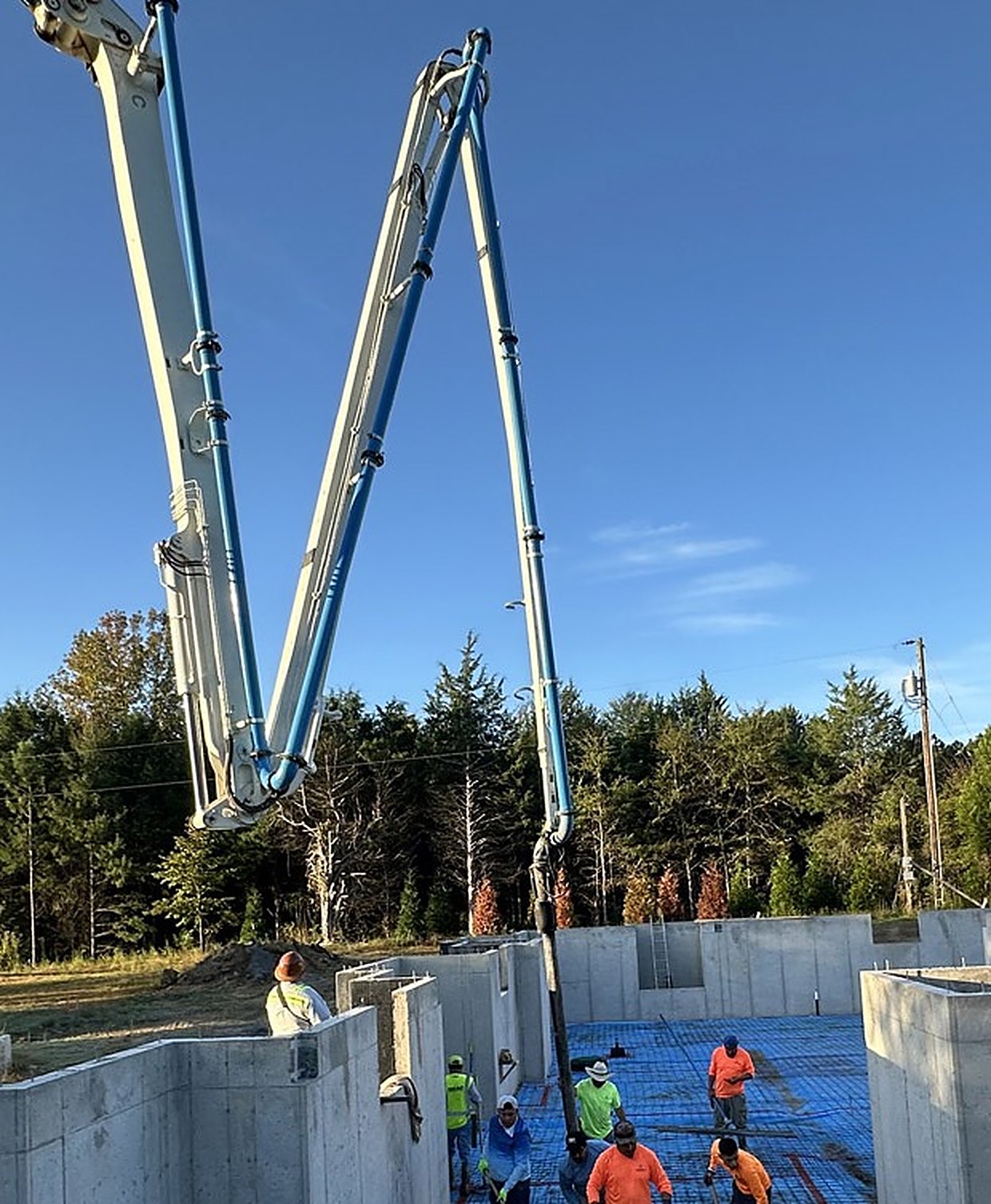 Two boom pump arms converging over a foundation, crew placing the slab between poured walls below